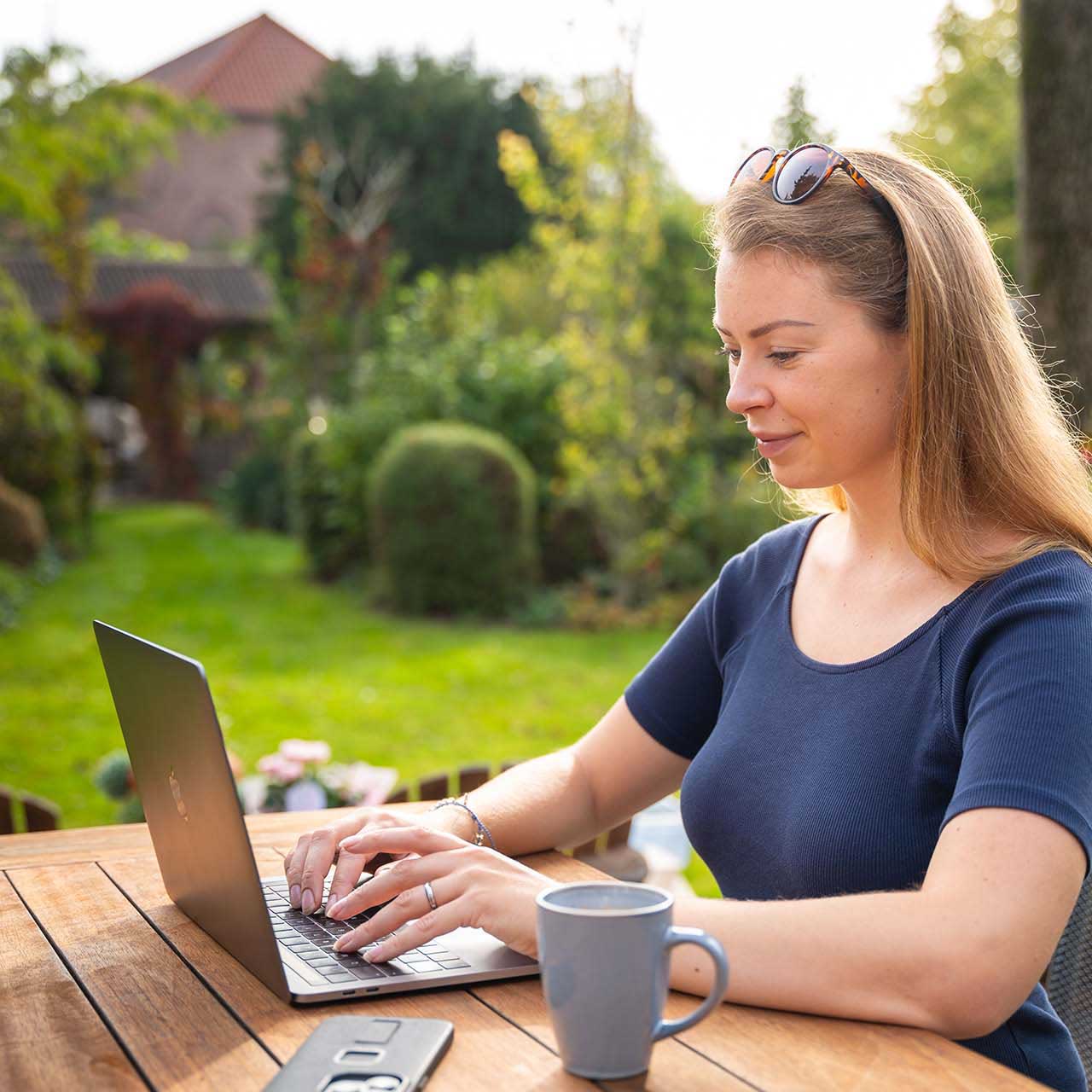 Nadia achter laptop met een mooie groene tuin op de achtergrond